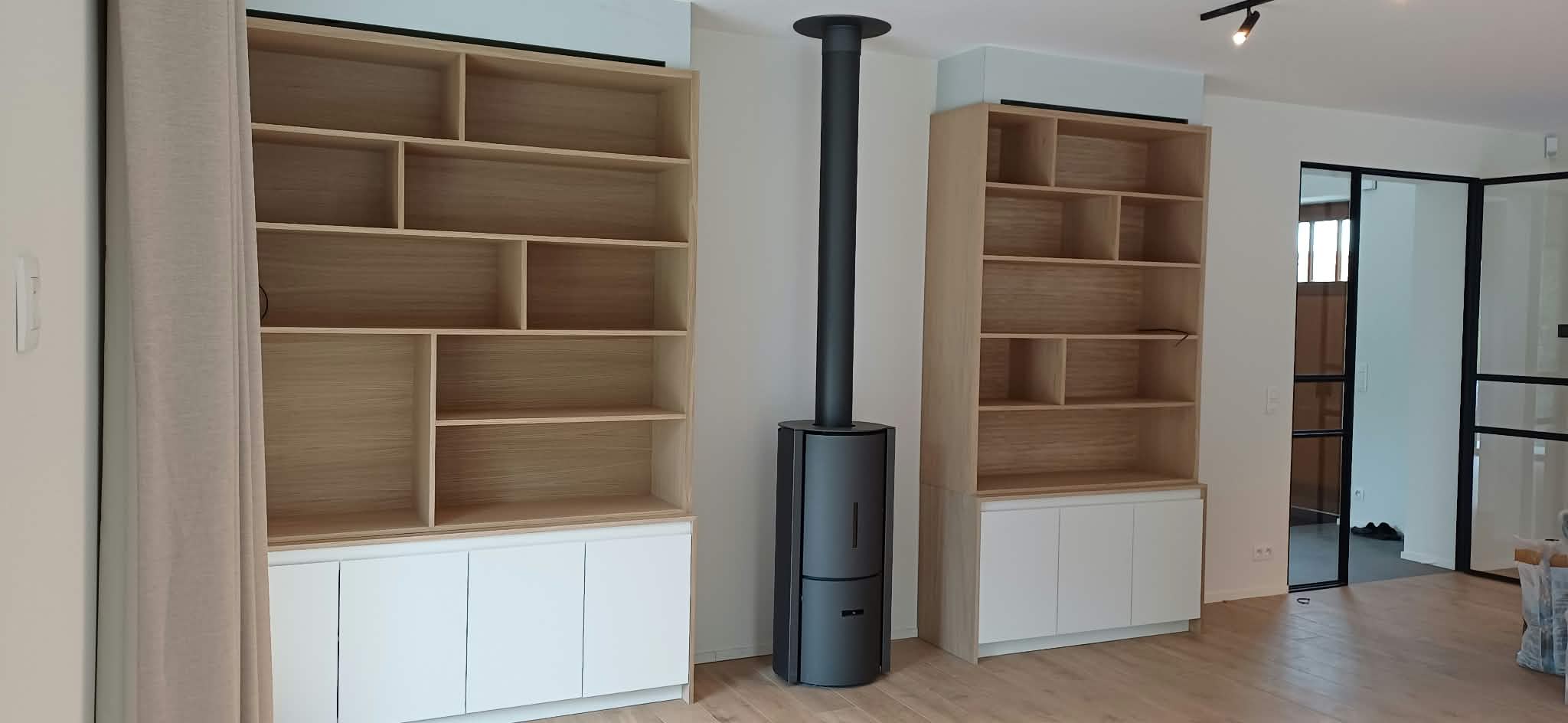 Deux bibliothèques en bois clair avec rangements bas autour d'un poêle